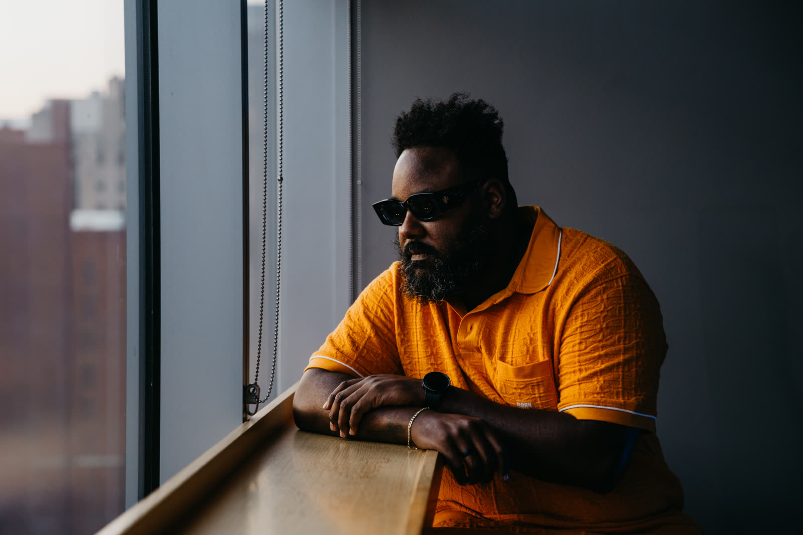 thatjermaine.wav — leaning at a window, contemplative, terracotta polo